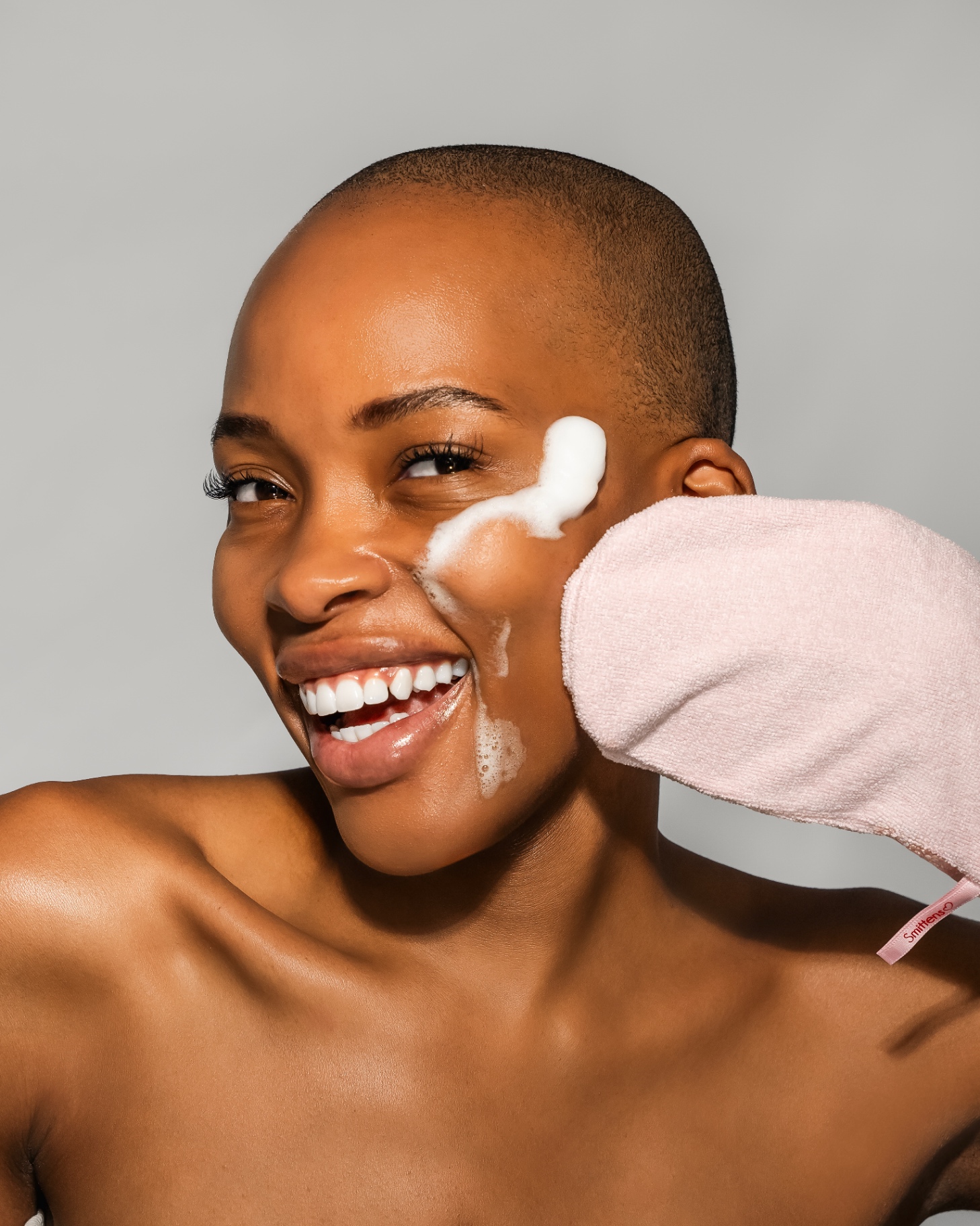 Smiling woman cleansing her face with a pink Smittens microfibre mitten